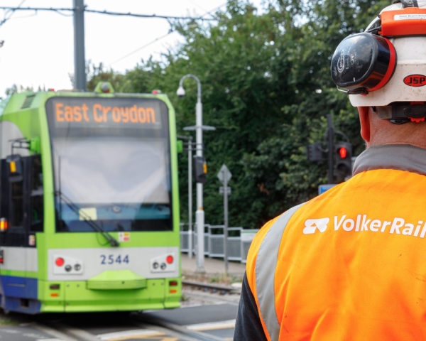 VolkerRail logo on back of a mans PPE with East Croydon tram in the background